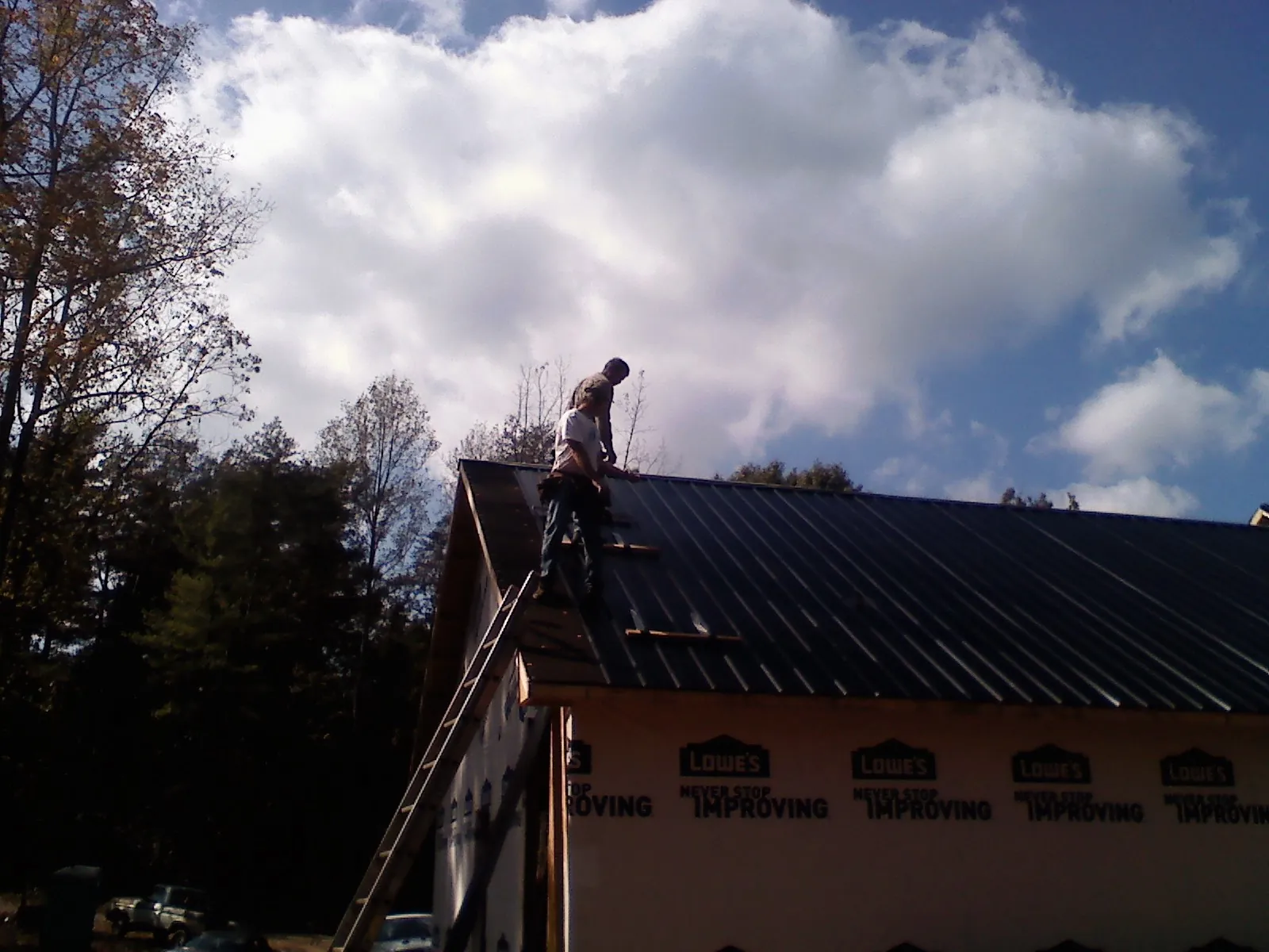 Roofer fastening dark metal panels high against a cloudy sky, from a Roof Inspection job in New Vienna