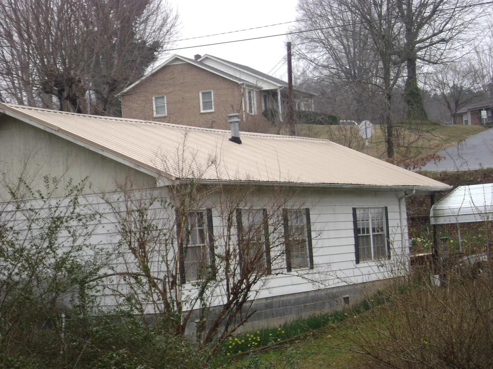 Tan metal roof on a white sided house set into a hillside — Commercial Roofing by Roofing Brothers in New Vienna